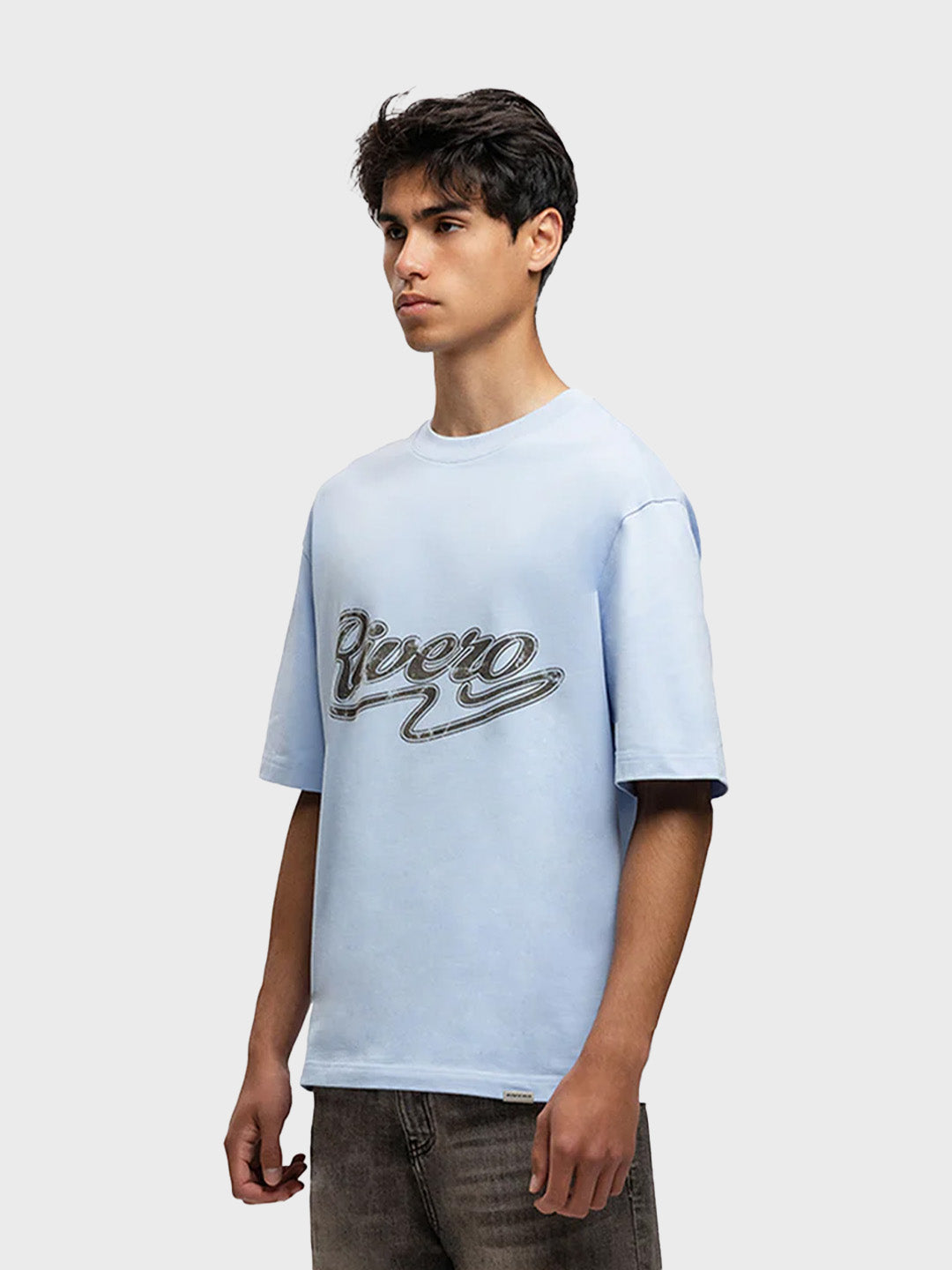 Model draagt Rivero Script T-Shirt in lichtblauw – schuin vooraanzicht