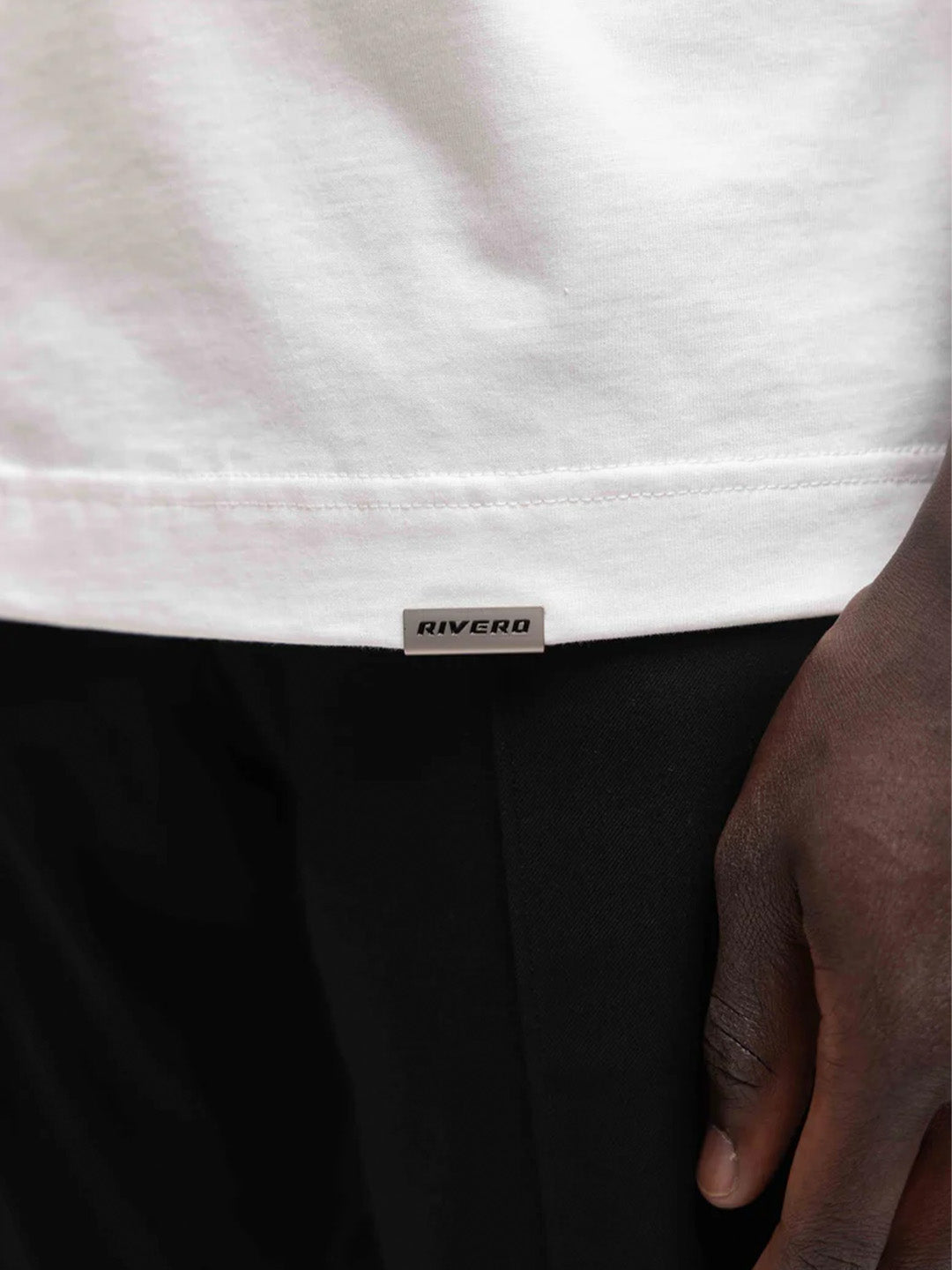Detail van het metalen Rivero-label rechtsonder op het t-shirt