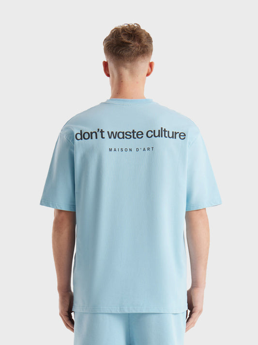 Model draagt Don’t Waste Culture Cleo T-shirt in light blue, rugzijde zichtbaar met grote graphic