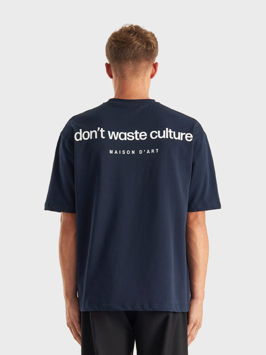 Model draagt Don’t Waste Culture Cleo T-shirt in Navy, rugzijde zichtbaar met grote graphic