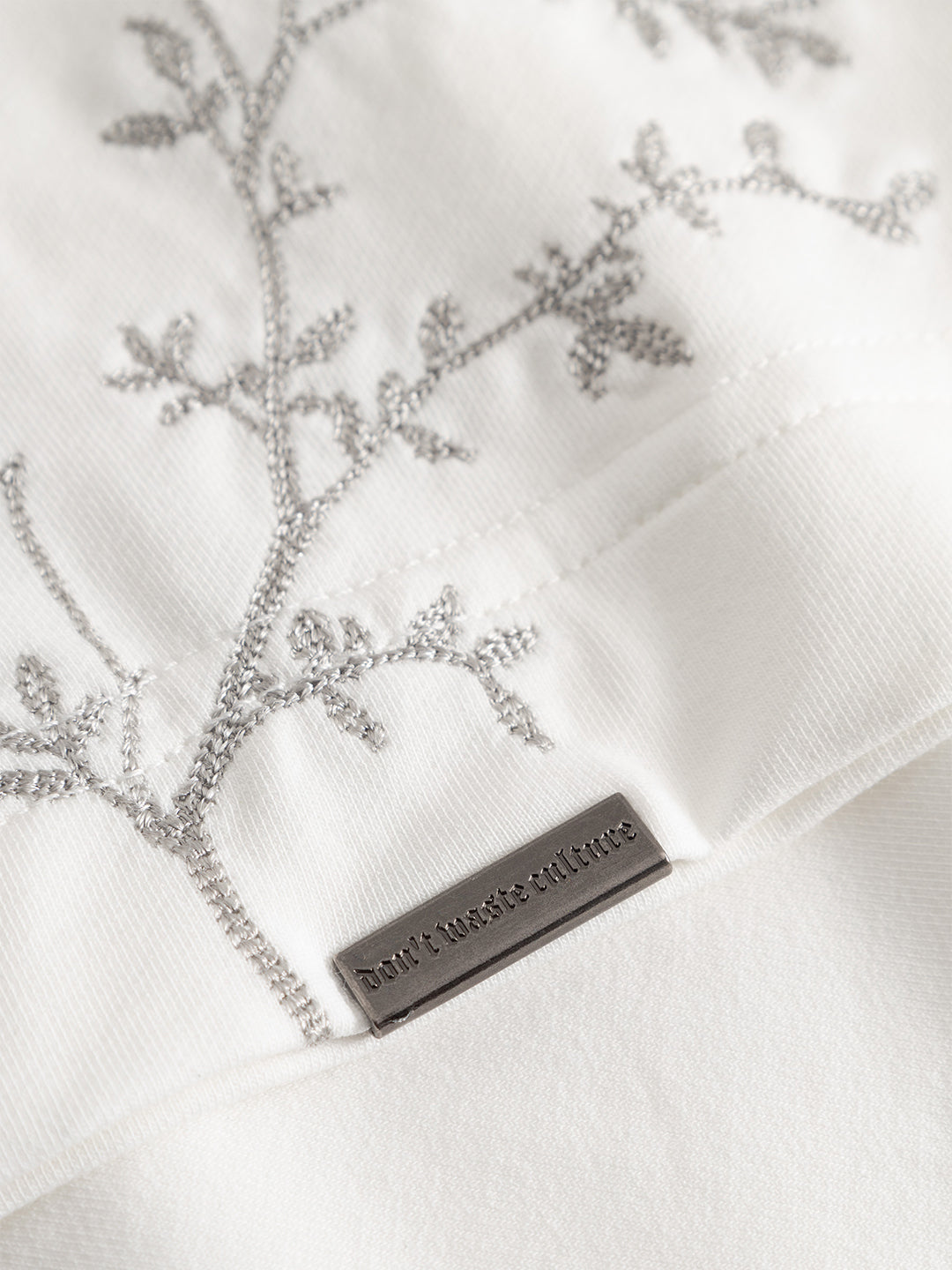 Close-up geborduurde olijftakken en metalen label DWC Morikae T-Shirt