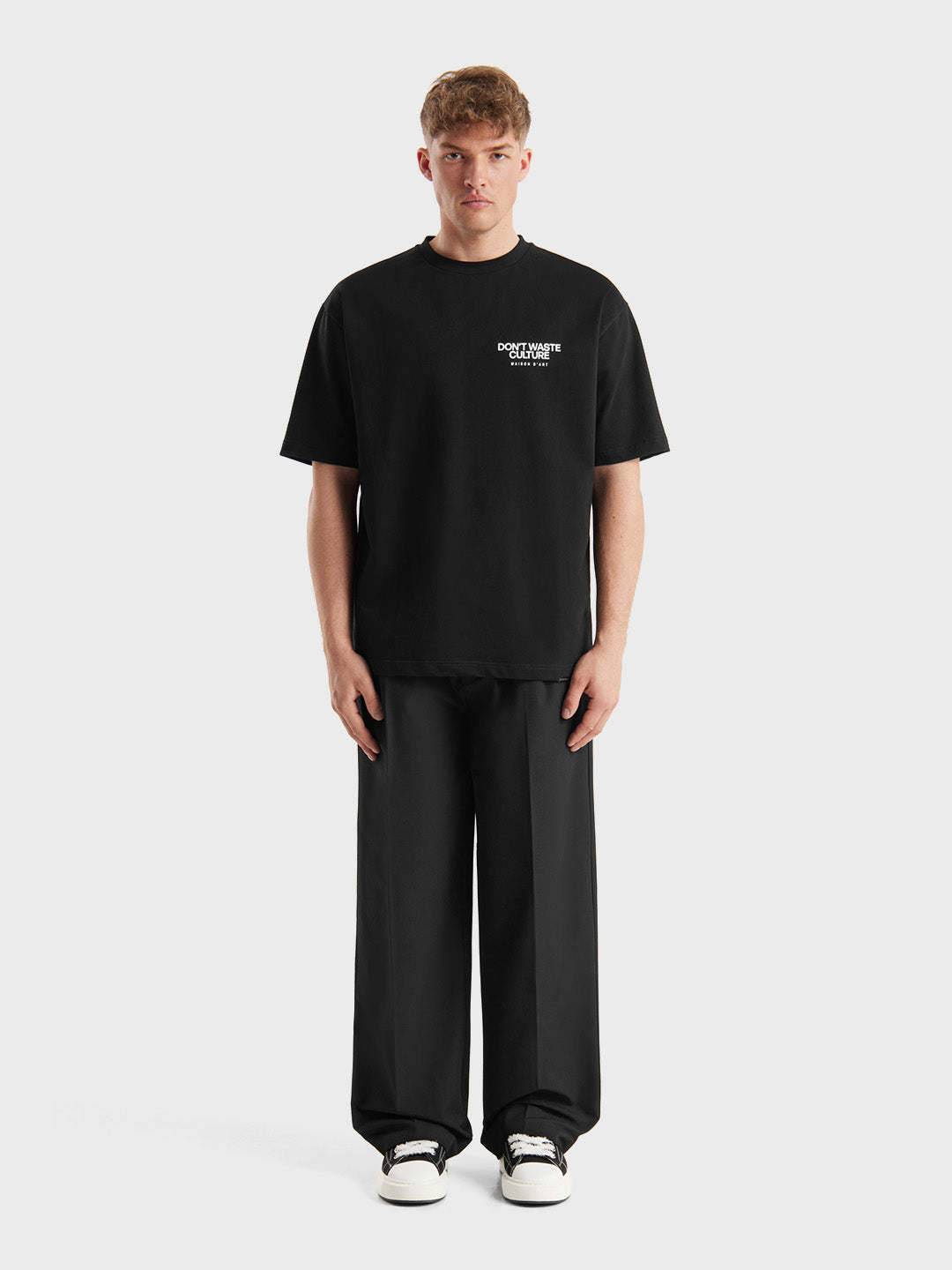Model draagt zwart Tirion T-shirt van DWC met wijde pantalon en sneakers, volledige outfit.
