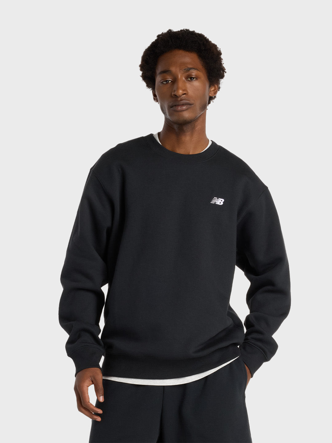Vooraanzicht van model met zwarte New Balance crewneck en subtiel borstlogo