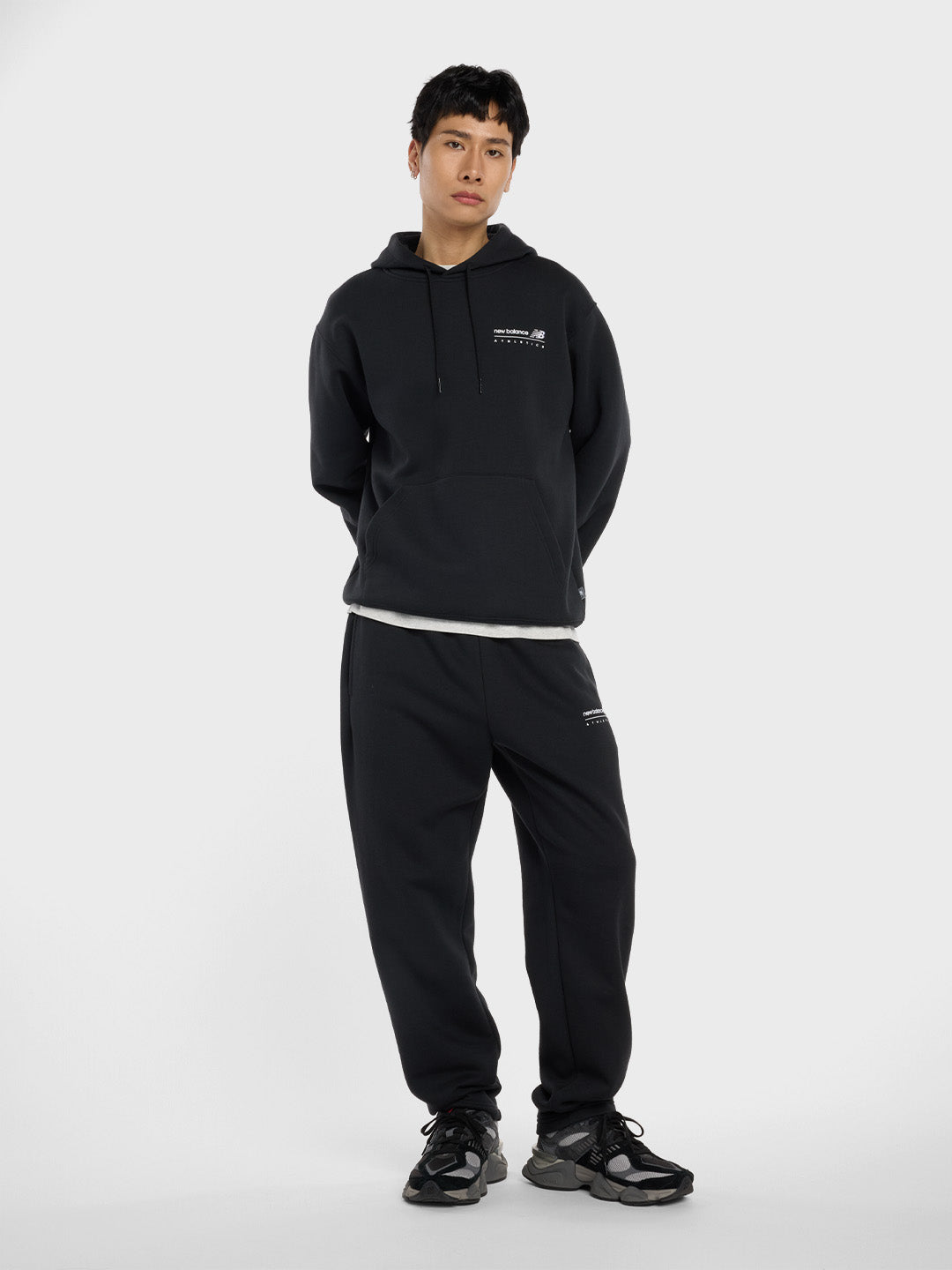 Model draagt volledige New Balance set met zwarte sweatpants, hoodie en 9060 sneakers