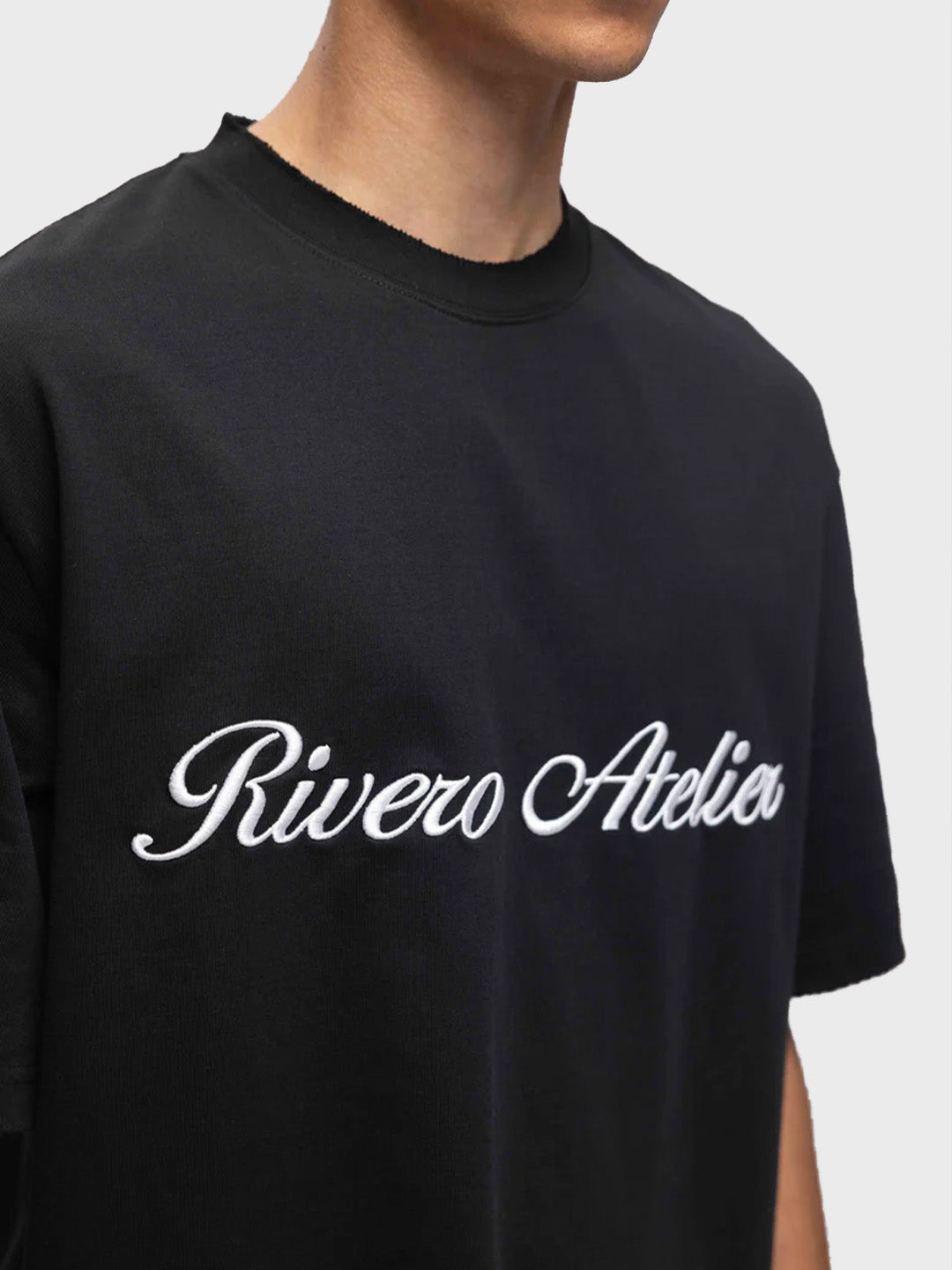 Close-up van geborduurde Rivero Atelier graphic op zwarte T-shirt