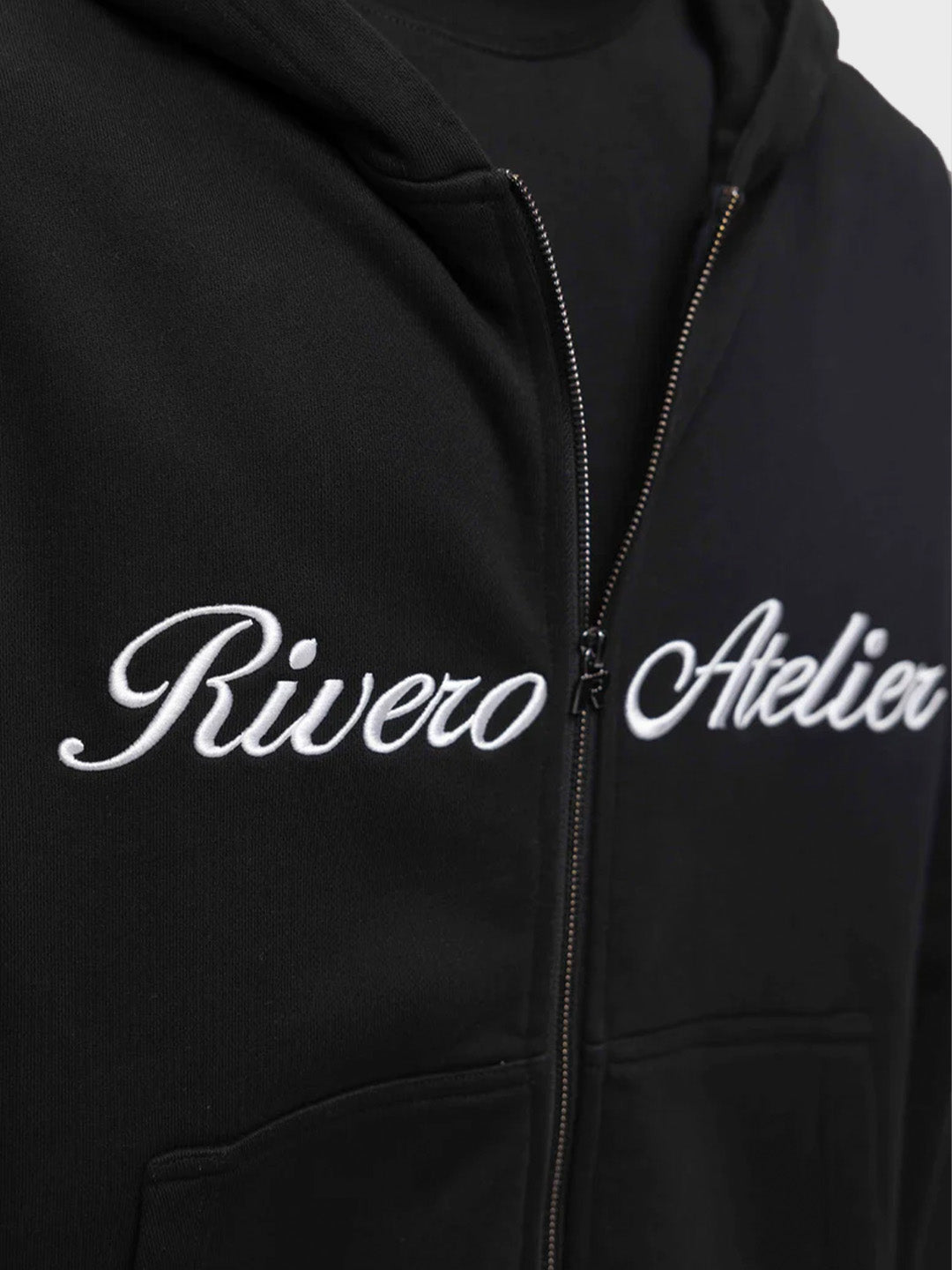 Close-up van geborduurde Rivero Atelier graphic op zwarte hoodie