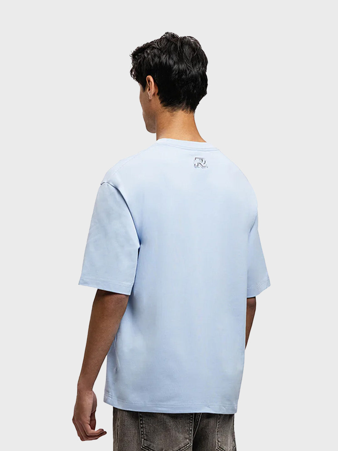 Model draagt Rivero Script T-Shirt in lichtblauw – schuin achteraanzicht