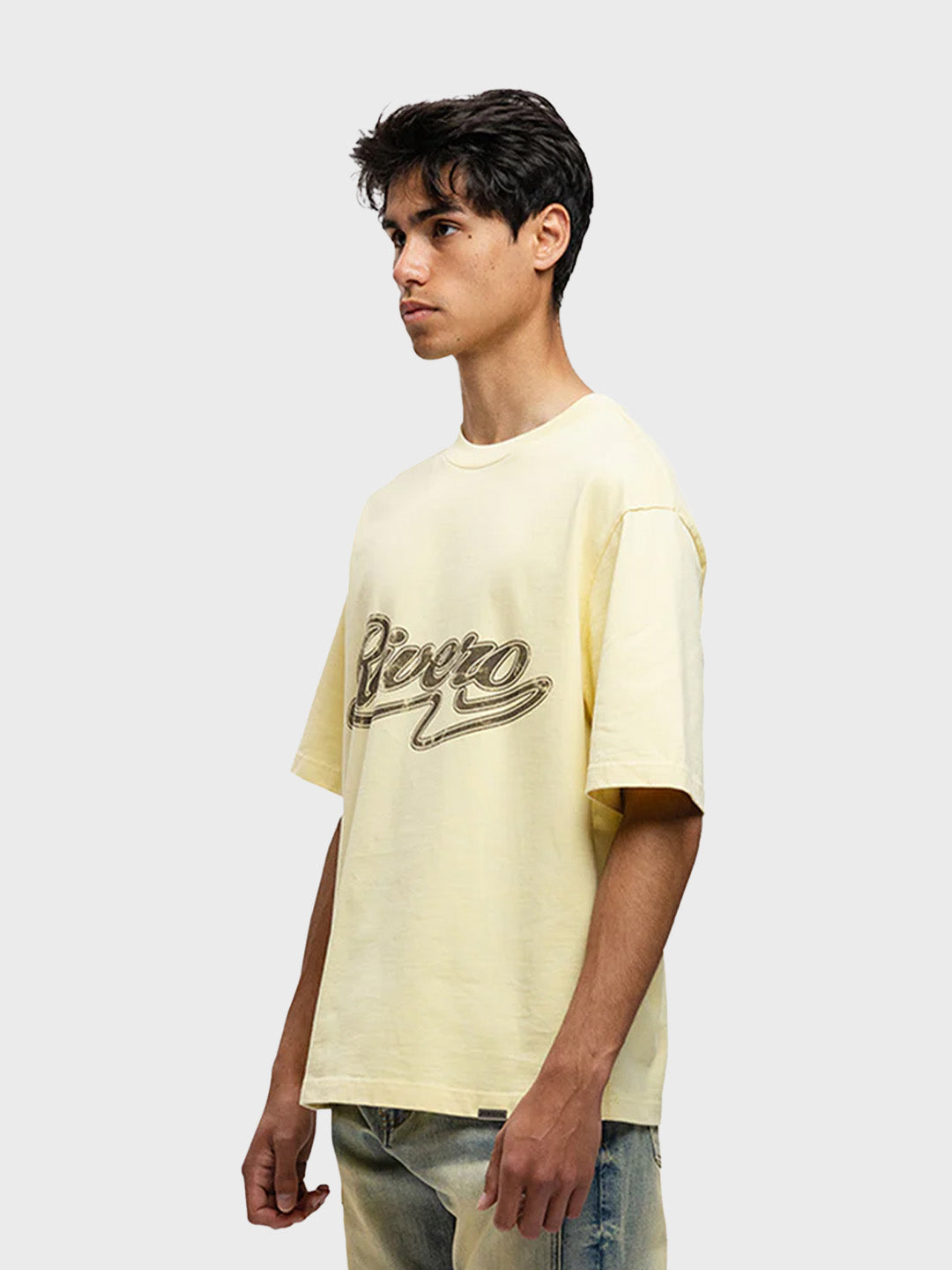 Model draagt Rivero Script T-Shirt in zachtgeel – schuin vooraanzicht