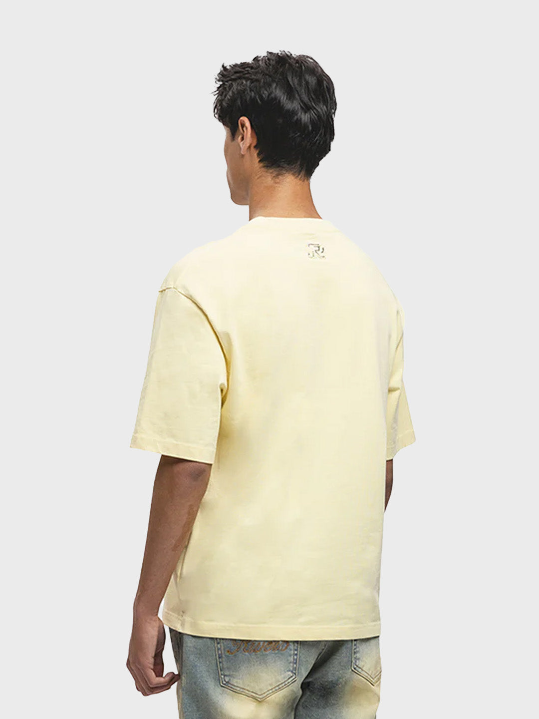 Model draagt Rivero Script T-Shirt in zachtgeel – schuin achteraanzicht